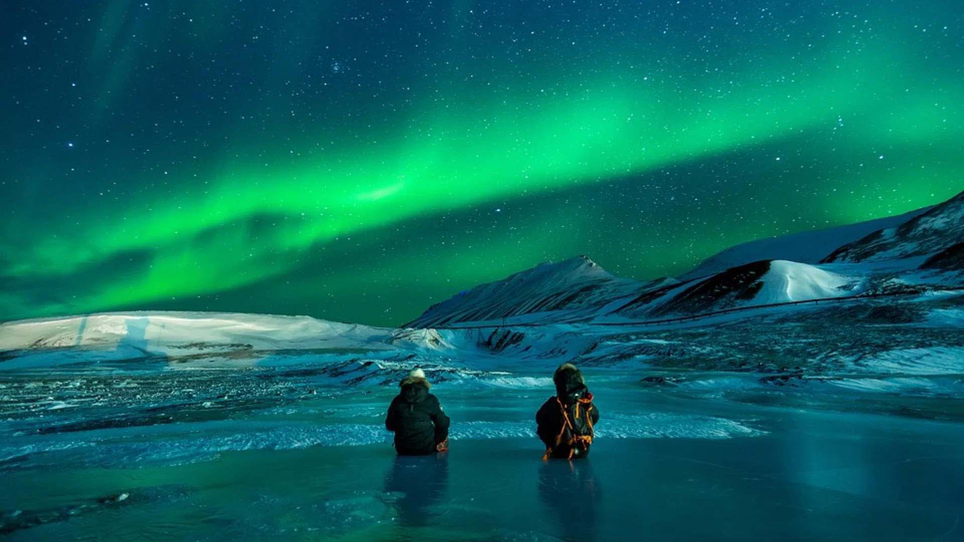 2 persone ammirano seduti l'aurora boreale alle svalbard