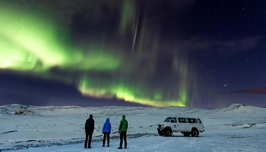 3 uomini vicino ad una superjeep su un ghiacciaio in Irlanda sotto l'aurora boreale